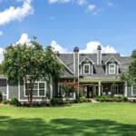 The rear view of a large gray craftsman new construction house with a landscaped yard and a garage and driveway