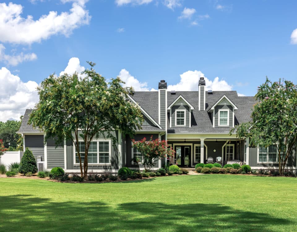 The rear view of a large gray craftsman new construction house with a landscaped yard and a garage and driveway